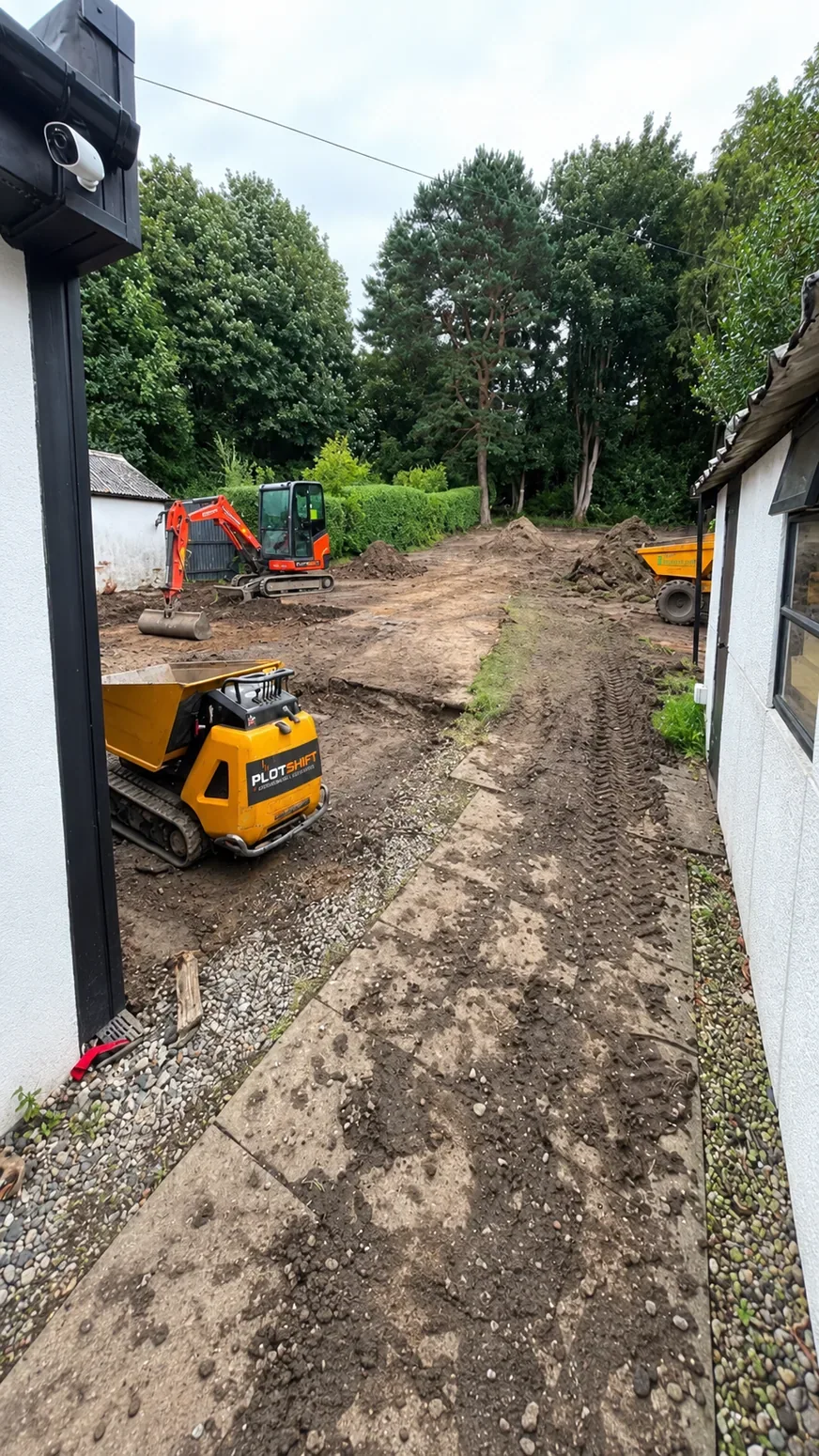 Compact excavator and dumper working on ground preparation at a residential site